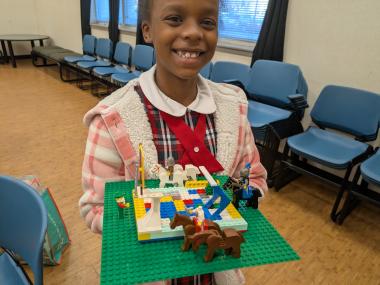 A smiling girl holds up a Lego creation.