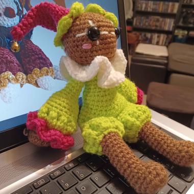 A little crocheted jester with tan skin, it's clothes pink and lime green